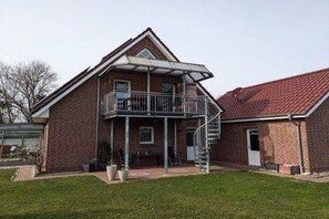 Ein zweistöckiges Backsteinhäuschen mit Balkon, überdachter Terrasse und kleiner angebauter Garage.