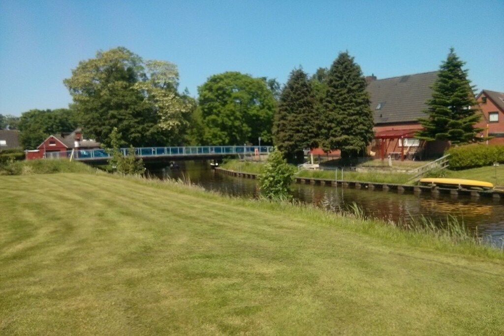 Une zone herbeuse avec un pont, une étendue d’eau et des maisons en arrière-plan.