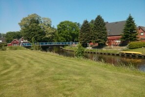 A grassy area with a bridge, a body of water, and houses in the background. - Biesterfeld holiday apartment (Bedekaspeler Marsch  \/ Südbrookmerland)