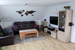 A living room with a dark brown sofa, a wooden coffee table, a world map wall decoration, a TV, and a wooden cabinet with glass doors. - Biesterfeld holiday apartment (Bedekaspeler Marsch  \/ Südbrookmerland)