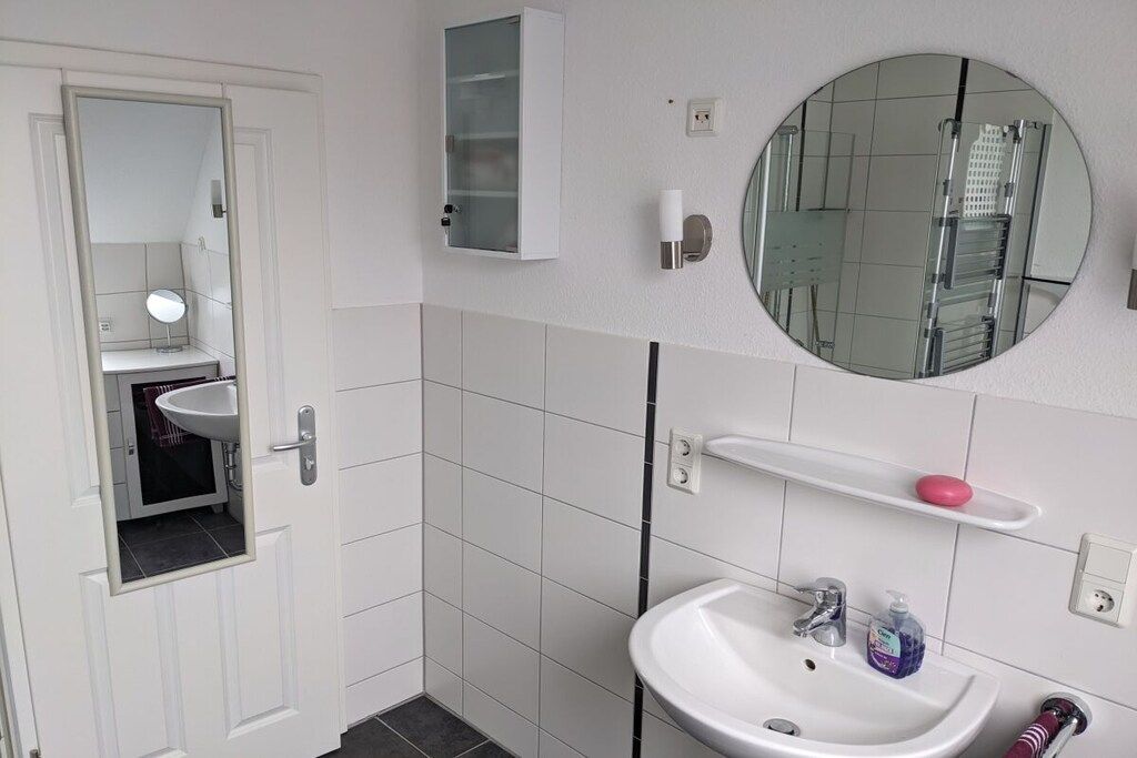 A bathroom with a white sink, a mirror, a medicine cabinet, and a round mirror on the wall.