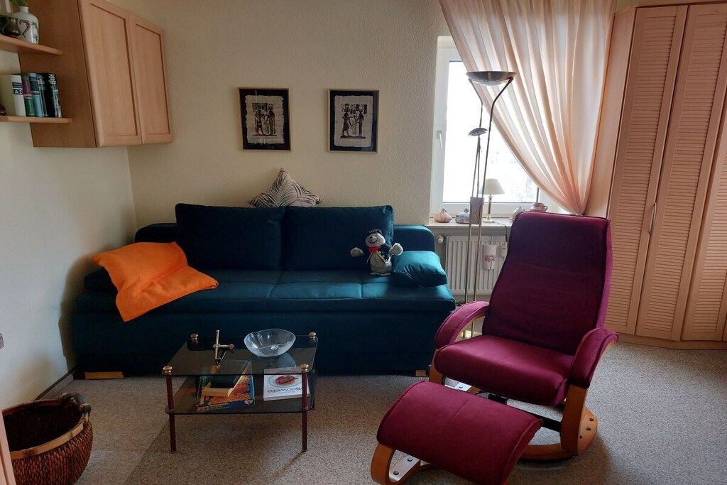 Una sala de estar con un sofá azul oscuro, un sillón mecededor rojo, una mesa de centro de vidrio y una estantería.