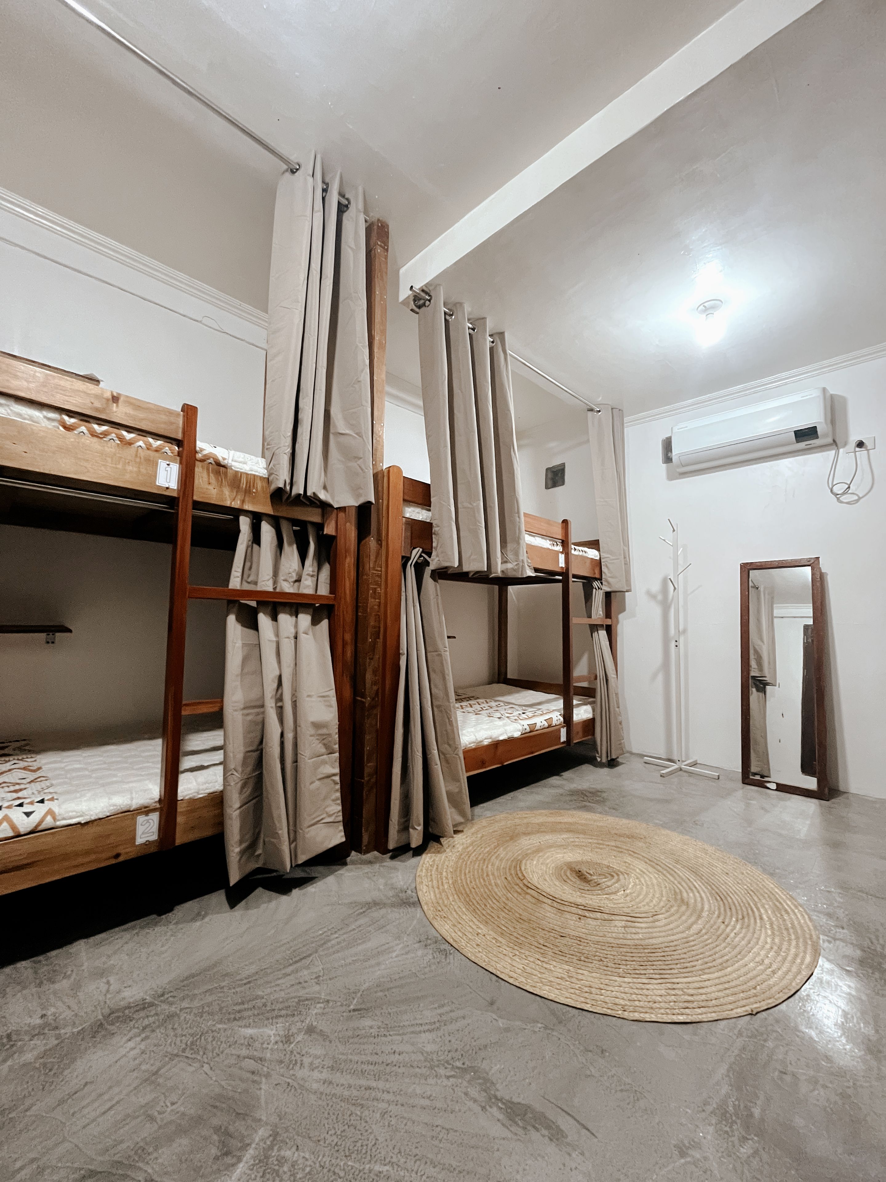A dormitory room with bunk beds, a woven rug, and an air conditioning unit.