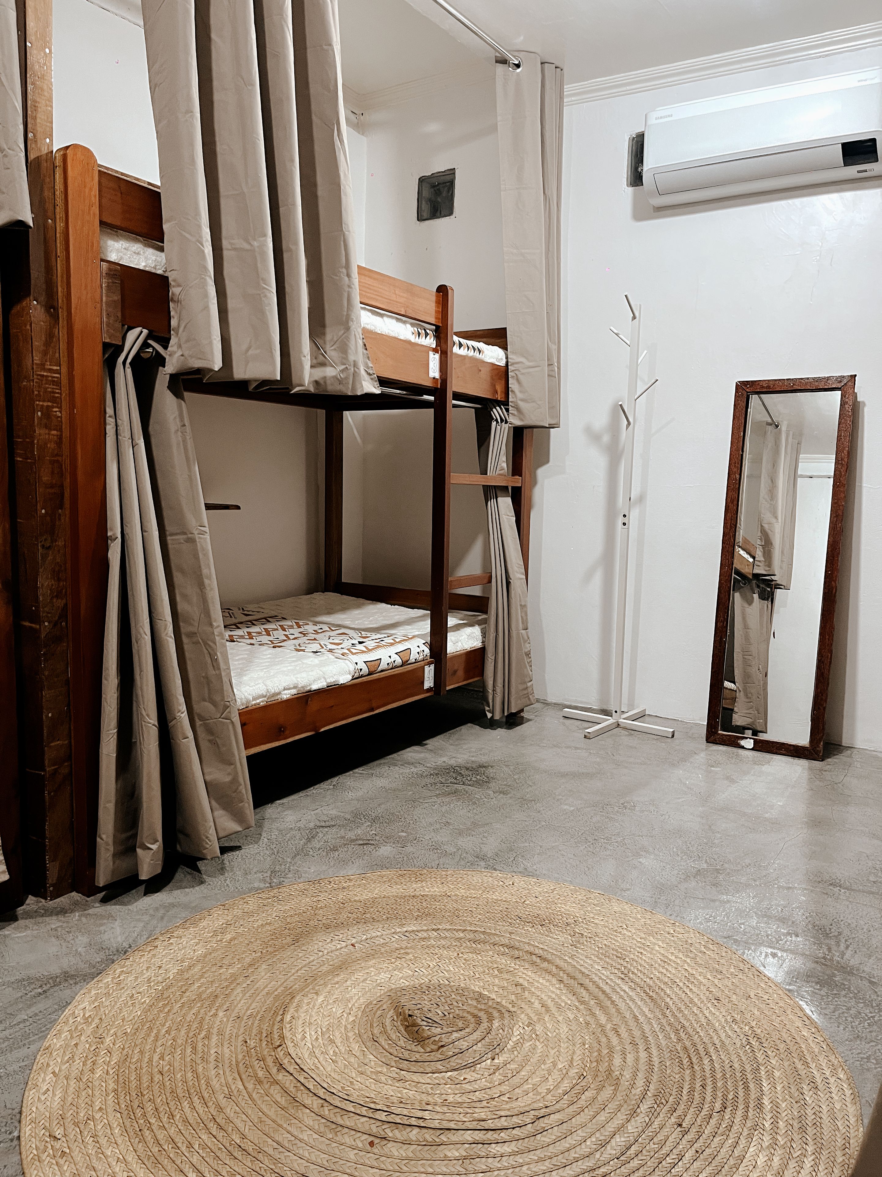 Una cama individual con colchón, un tapete tejido, un espejo y un equipo de aire acondicionado.