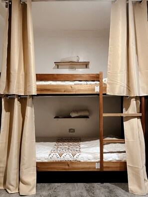 A bunk bed with a wooden frame, a small shelf above the top bunk, and a patterned pillow on the lower bed. - The Eight Siargao (General Luna)