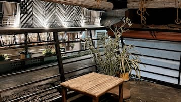 Una mesa de madera con dos cojines, una planta en maceta y una barandilla con vista a la calle.