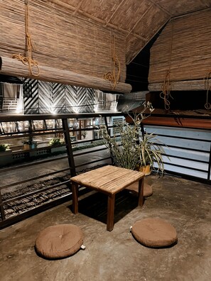 A wooden table with two cushions, a potted plant, and a railing overlooking a street.