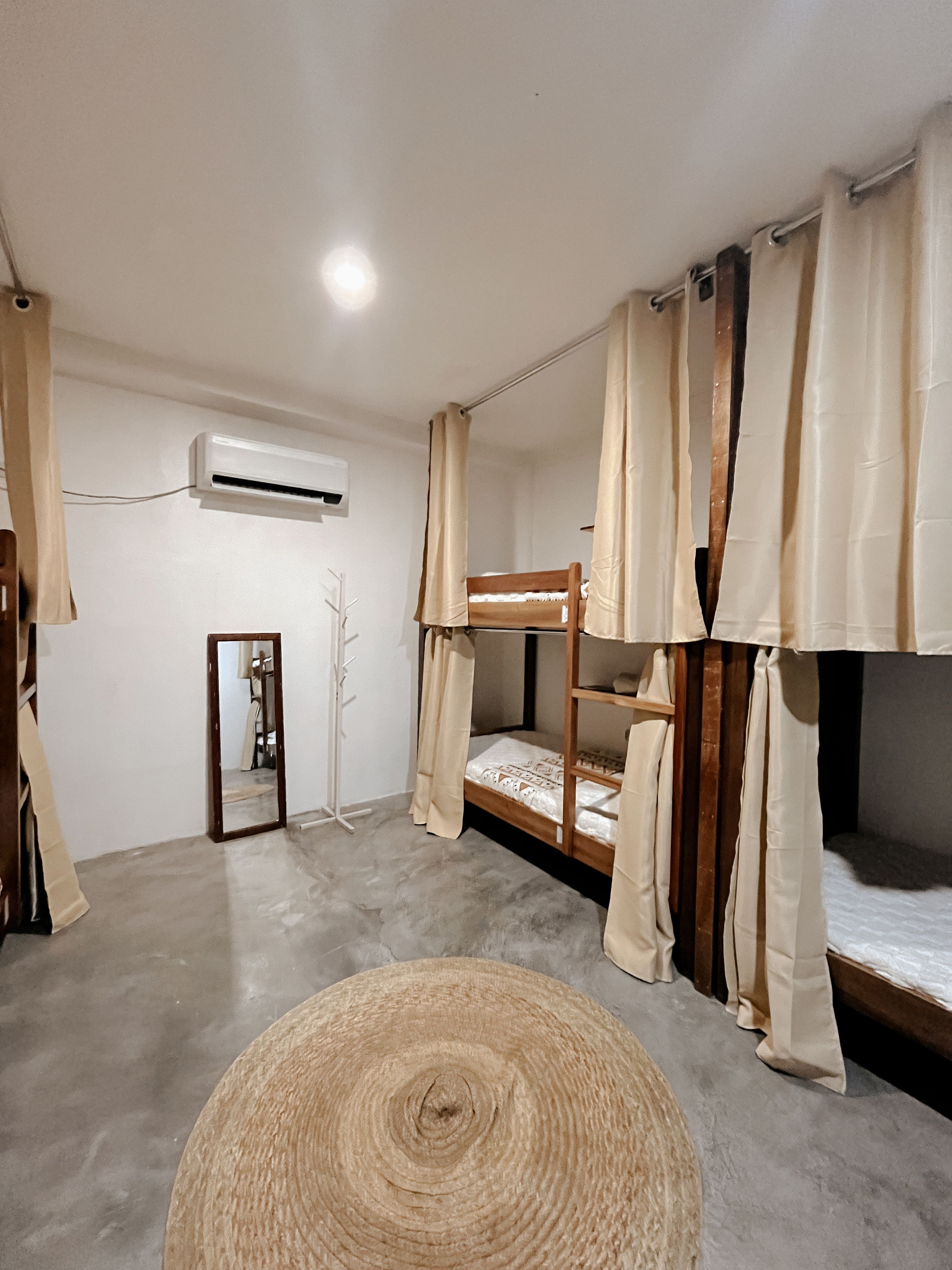 A room with bunk beds, a standing mirror, and an air conditioning unit.