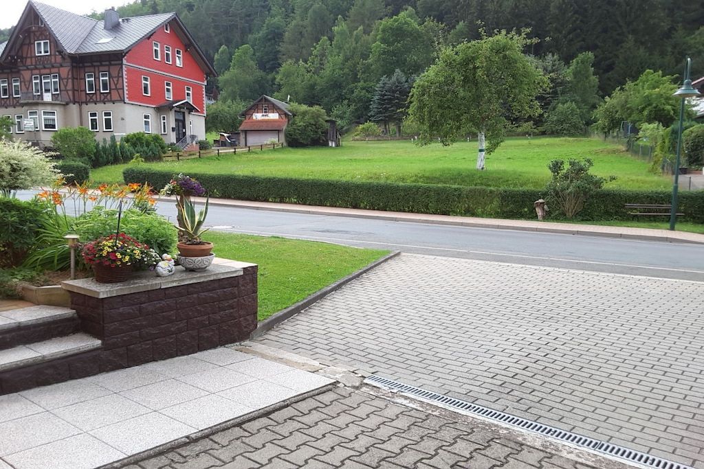 A residential area with a paved driveway, a large house with a red facade, and a well-maintained lawn.