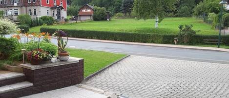 Un barrio residencial con entrada pavimentada, una casa grande de fachada roja y un césped bien cuidado.