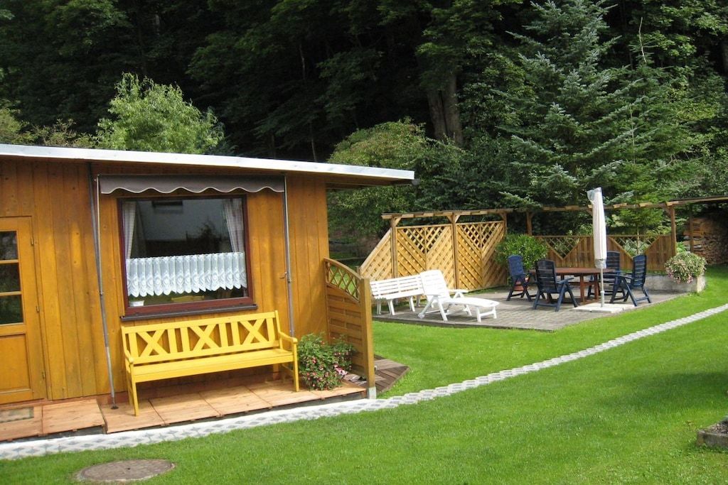 A wooden cabin with a porch, a bench, and a table with chairs.