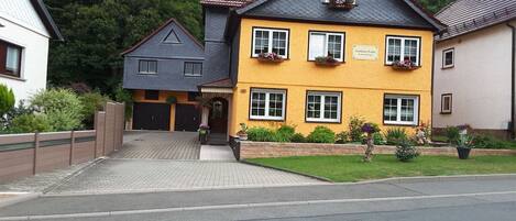 A two-story building with a yellow facade, a black roof, and a paved driveway leading to the entrance.