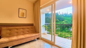 Quarto com sofá, quadro na parede e varanda com vista para vegetação.
