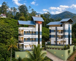 A hotel with a modern design, featuring multiple floors and balconies, set against a lush green hillside.