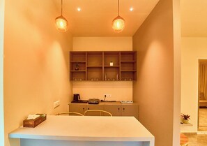 A compact kitchen with a white countertop, two pendant lights, and a built-in shelf unit above.