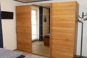 A room with a sliding wooden wardrobe, a bed with striped bedding, a floor lamp, and a television mounted on the wall. - BOOTY 55, "Am Stadtwald", Apartment 9 (Kühlungsborn)
