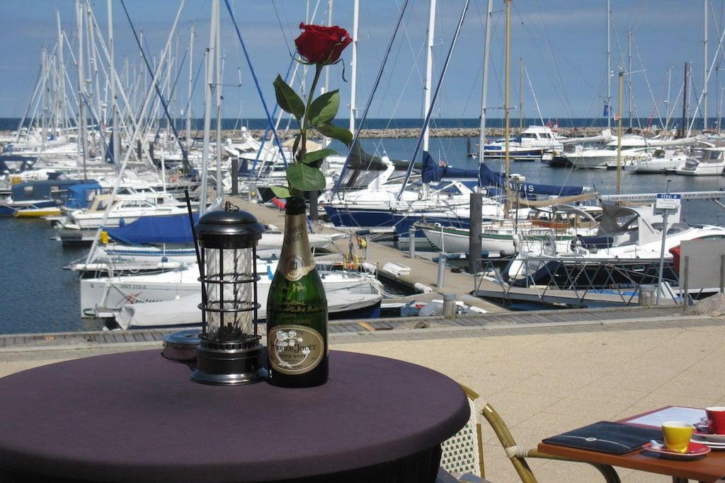 A table with a bottle and a rose, overlooking a marina with boats.