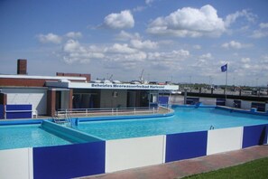An outdoor swimming pool with a blue and white color scheme, surrounded by a low brick wall. - Holiday apartment with 2 bedrooms (Carolinensiel)