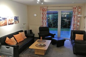 A living room with a sofa, armchairs, a coffee table, and a view through a glass door to the outside. - Holiday apartment with 2 bedrooms (Carolinensiel)