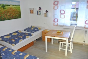 Ein Schlafzimmer mit einem Bett, einem Schreibtisch und einem Stuhl. Ein Fenster mit Vorhängen und eine Heizung sind ebenfalls vorhanden.