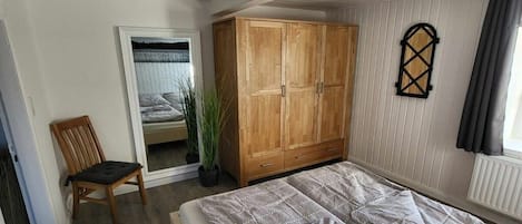 Een slaapkamer met een bed, een houten garderobe, een stoel, een kamerplant en een raam met gordijnen.