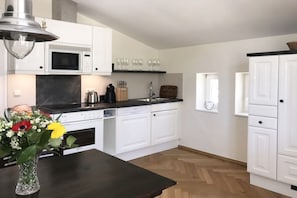 A modern kitchen with white cabinets, a microwave, a sink, and a window. - Villa Achterkerke / 1st floor (Seebad Heringsdorf)