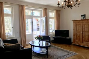 A living room with a sofa, a glass coffee table with a vase, a TV, and a wooden cabinet. - Villa Achterkerke / 1st floor (Seebad Heringsdorf)