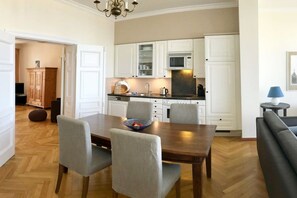 Een kleine keuken met witte kastjes, een magnetron en een eethoek met een houten tafel en vier stoelen.