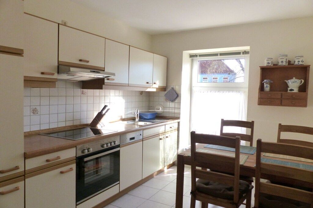 Una cocina con armarios blancos, una estufa y un ventanal con vistas a una casa.