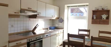 A kitchen with white cabinets, a stove, and a window with a view of a house.