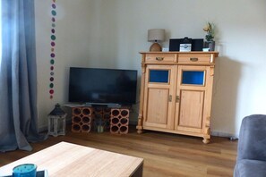 A living room with a flat-screen TV, wooden cabinet, and a coffee table. - Holiday apartment with 1 bedroom (Hooksiel)