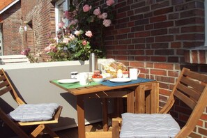 An outdoor dining area with a brick wall, wooden table, and chairs. - Holiday apartment with 1 bedroom (Hooksiel)