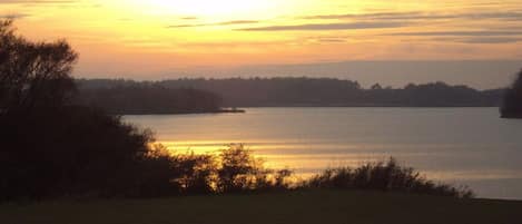 A lake at sunset with a clear sky, surrounded by trees and vegetation.