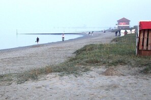 Een strand met een houten constructie, een redershut en een zandpad dat naar het water leidt.