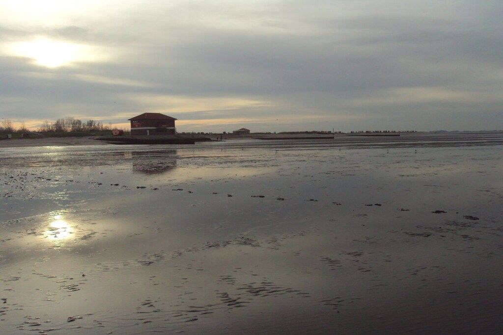 A building with a flat roof and a rectangular shape, situated on a wet surface that reflects the sky.