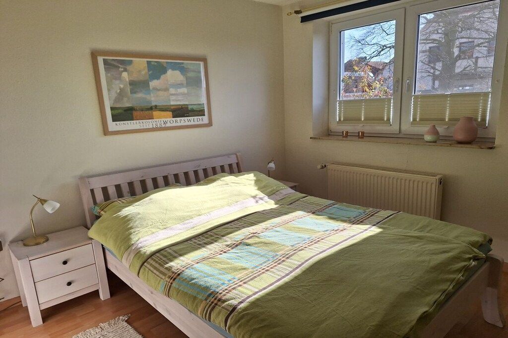 A bedroom with a bed, a nightstand, a window with blinds, and a framed picture on the wall.