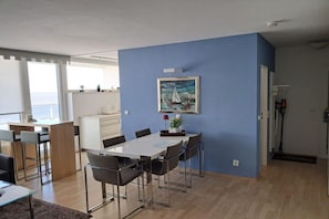 Ein modernes Wohnzimmer mit Essbereich, einem Gemälde an der Wand und Meerblick durch große Fenster.