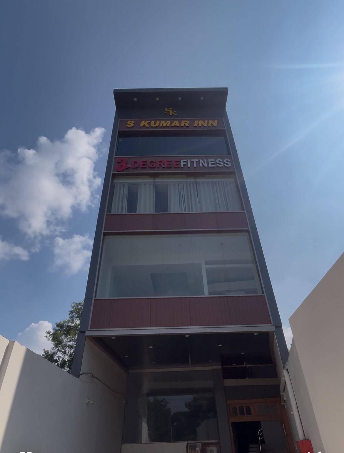Ein Gebäude mit Schildern für 'S Kumar Inn' und 'Degree Fitness', das ein Hotel und ein Fitnesscenter kennzeichnet.