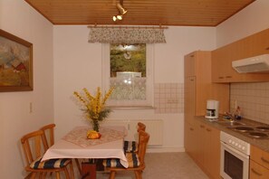 A kitchen with wooden cabinets, a dining table with chairs, a window with a view, and a radiator. - Holiday apartment with 2 bedrooms (Bad Schandau)