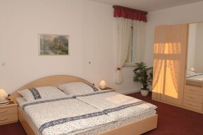 A bedroom with a bed, bedside table, lamp, potted plant, wardrobe, and a window with curtains. - Holiday apartment with 2 bedrooms (Bad Schandau)