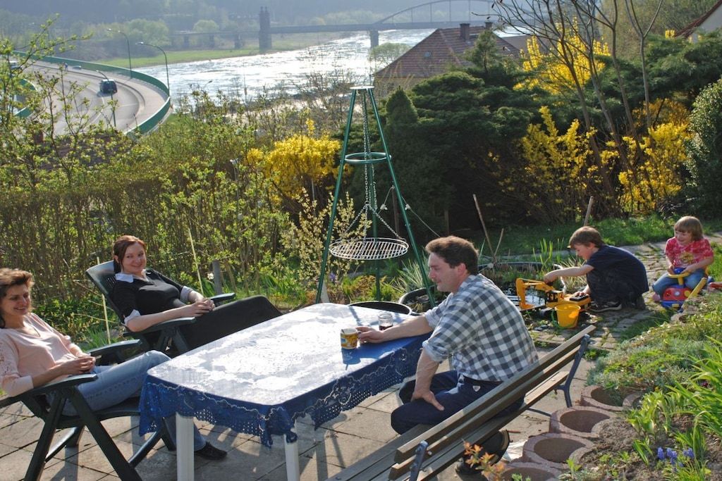 Un groupe de personnes est assis autour d’une table à l’extérieur, avec une rivière et de la verdure en arrière-plan.