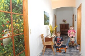 A hallway with a window view of a garden, a wooden chair, a small table with a vase of flowers, and a door at the end. - Holiday apartment with 2 bedrooms (Bad Schandau)