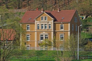 Um edifício de vários andares com fachada simétrica, entrada central e telhado de telhas vermelhas.