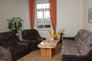 A living room with two dark patterned sofas, a coffee table with magazines, a potted plant, and a window with curtains. - Holiday apartment with 2 bedrooms (Bad Schandau)