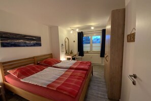 Een slaapkamer met twee bedden, een houten garderobe, een bureau met stoel, een raam met gordijnen en een schilderij aan de muur.