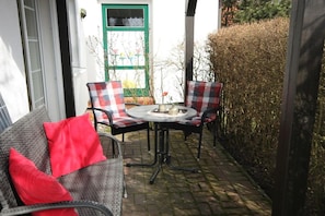Eine Terrasse mit einem Korbsessel, zwei karierten Sesseln und einem kleinen runden Tisch.