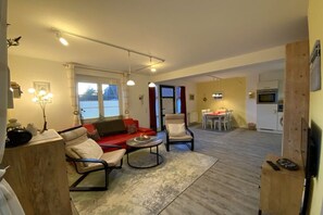 Een woonkamer met een rode bank, twee fauteuils, een salontafel, en een eethoek met een tafel en stoelen.