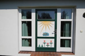 Eine Tür mit Sonn- und Tulpendekor, ein Fenster mit Vorhängen und ein Backsteinbordsitz.