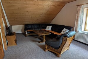 Ein Loft-Zimmer mit schräg verlaufender Decke, einer schwarzen Ledersofa, einem Holztisch und einem Holzsesseln.
