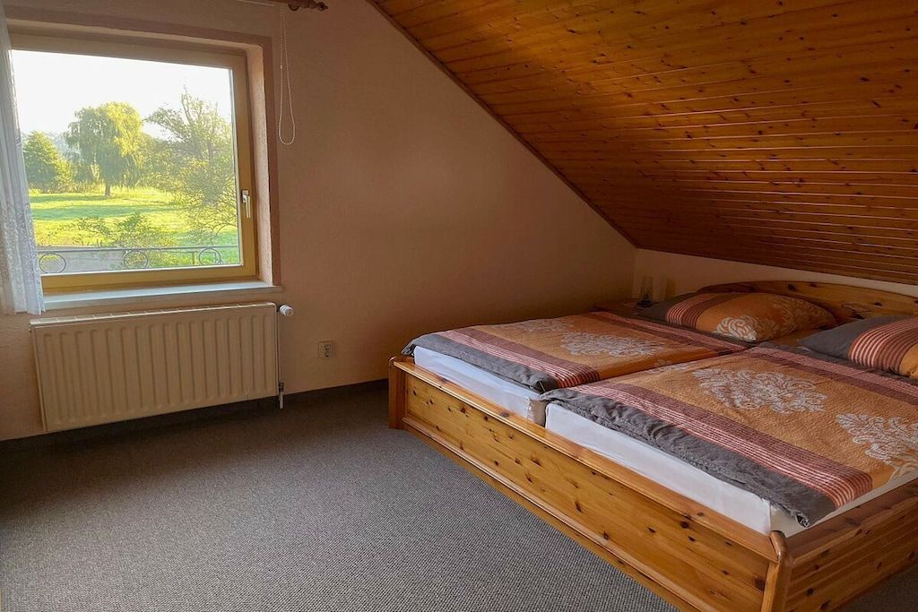 A bedroom with a sloped ceiling, a wooden bed, a window with a view of greenery, and a radiator.